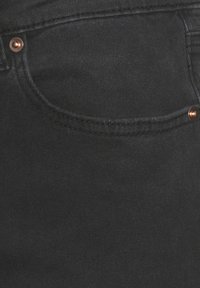 Melna džinsa audums ar gludu tekstūru, kuram ir maza priekšējā kabata un vara kniedes piešuvēm.