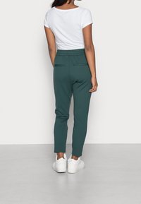 Mörkgröna joggers med avspänd passform, elastisk midja och två bakfickor, i kombination med en vit t-shirt med kort ärm och vita sneakers.