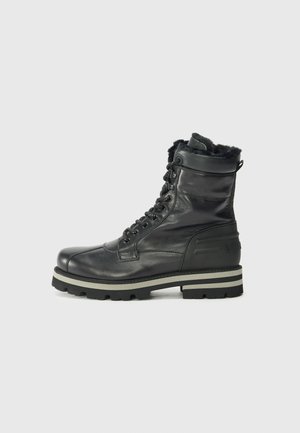 Schwarze Lederstiefel mit Fellfutter, Schnürung vorne und einer dicken, robusten Sohle mit einem grauen Streifen. Vor einem schlichten weißen Hintergrund platziert.