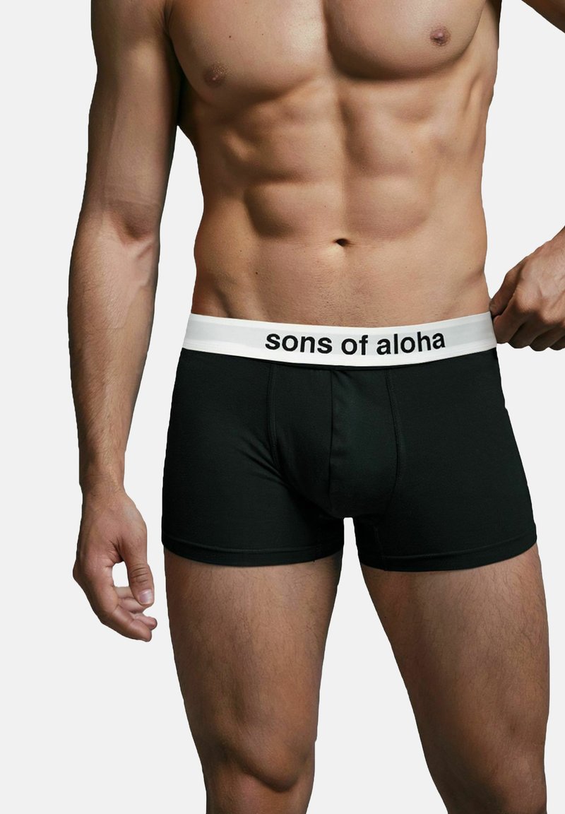 Boxer neri realizzati in un tessuto elasticizzato con una fascia bianca che mostra la scritta "sons of aloha" in carattere nero. Design aderente.