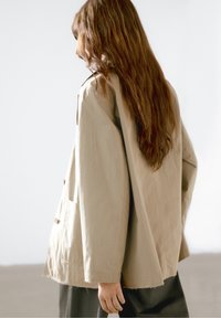 Beige bomulds overshirt med en afslappet pasform, store lommer og knaplukninger. Har en let frynset kant og lange ærmer.