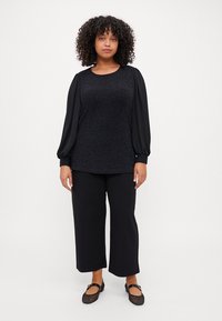 Black textured top with long, puffed sleeves, paired with wide-leg black pants. Model wears flat, black shoes with a round toe.