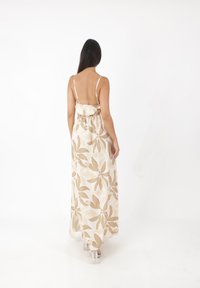 Robe maxi en tissu beige clair avec un motif floral ; dotée de fines bretelles et d'une taille cintrée, elle descend jusqu'aux chevilles.