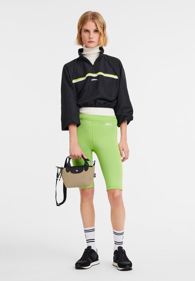 Black jacket with lime stripe, green biker shorts, black sneakers, white socks with black stripes, and a small beige bag with black accents.