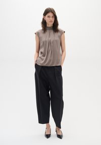 Maglietta senza maniche taupe elegante con pieghe, abbinata a pantaloni neri larghi e tacchi a punta neri. Finissaggio del tessuto semplice e liscio.