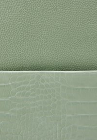 Zielona skóra z dwoma fakturami: górna część jest gładka i lekko chropowata, podczas gdy dolna ma błyszczący, przypominający alligator wzór.