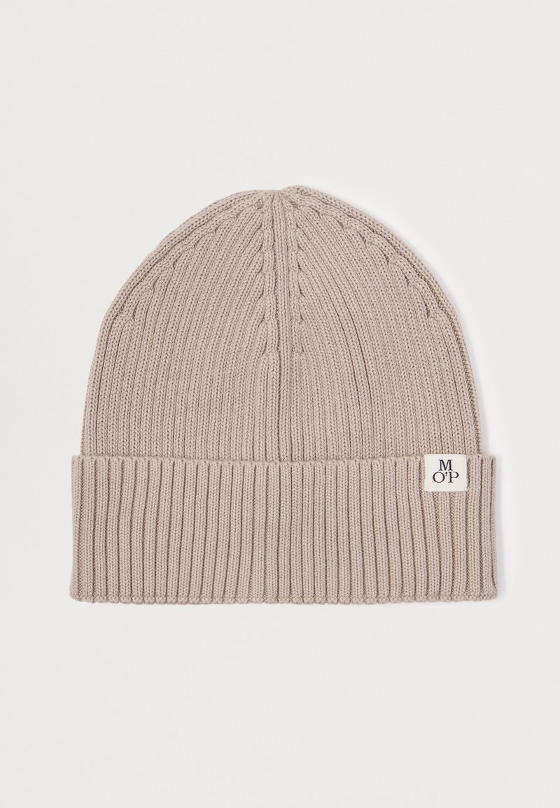 Knitted beanie in light beige with ribbed bottom. Features cable knit texture on top and a small brand tag on the side.