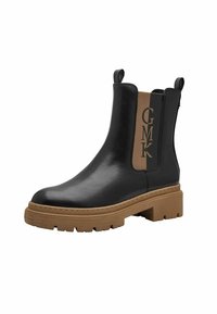 Bottines en cuir noir avec un panneau latéral élastique marron arborant l'inscription "GMK", semelle en caoutchouc texturée au design épais.