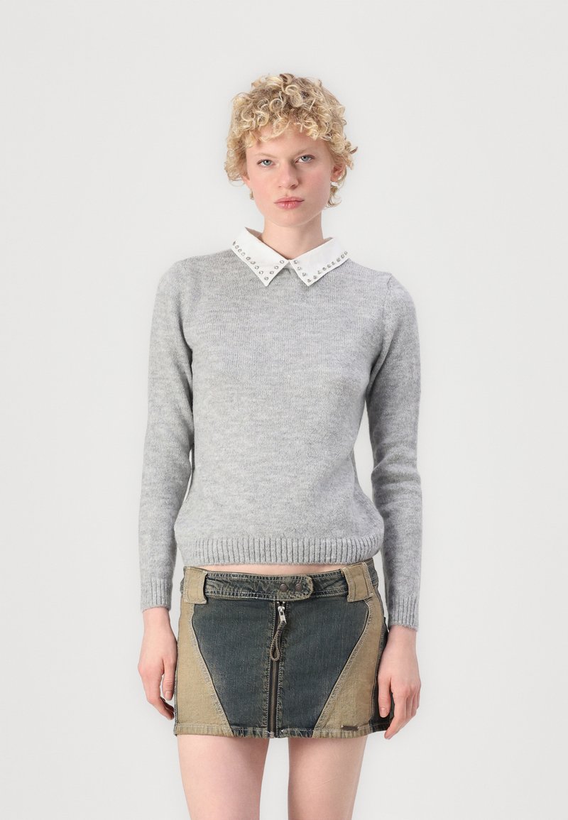 Pulover gri tricotat cu un guler alb ce are nasturi metalici. Modelul poartă o fustă mini din denim cu panouri contrastante și fermoar.