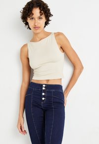 Világos bézs bordázott crop top sötétkék, magas derékú farmernadrággal, amely öt gombbal és kontrasztos varrási részletekkel rendelkezik.