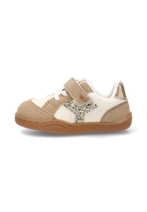 Zapatilla infantil beige y blanca con detalle de estrella brillante, cierre de velcro, cordones blancos, suela de goma y detalles de ante sobre un fondo blanco.