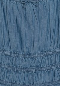Τζιν φόρεμα σε ανοιχτό μπλε χρώμα, με ελαστικές μαζεμένες λεπτομέρειες και κορδόνι στο πάνω μέρος. Μαλακή υφή και λεία φινιρίσματα.
