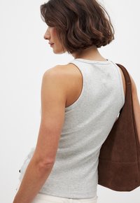 Débardeur gris côtelé avec un décolleté en forme de scoop, présentant une coupe ajustée. Le modèle porte un sac en suède marron à l'épaule.