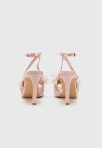 Pink satin high-heeled sandals with ankle straps, featuring delicate tulle accents and small pearls at the back. Smooth texture, open design.