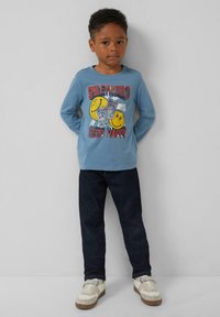 Blaues langärmliges T-Shirt mit grafischem Druck von Smileys und Text, kombiniert mit dunklen Jeans und weißen Sneakern. Schlichter, lässiger Stil.