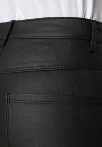 Μαύρο παντελόνι από ψεύτικο δέρμα με λεία υφή, διαθέτει μέση μεσαίου ύψους, πίσω τσέπες και διακριτές ραφές.