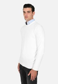 Maglione bianco a maglia con maniche lunghe e scollatura a girocollo, abbinato a una camicia colletto azzurra sottostante. Vestibilità slim, texture liscia.