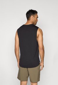 T-shirt noir sans manches en tissu doux, avec un col arrondi et des fentes sur les côtés, associé à un short beige.