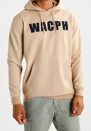 Sweatshirt beige à capuche avec "WACPH" en grandes lettres noires, doté d'une poche avant et d'un ourlet côtelé, fabriqué en tissu doux et extensible.