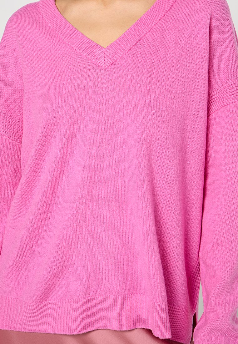Suéter de punto rosa con escote en V, corte relajado y puños acanalados. Fabricado en una textura suave con un ligero brillo.