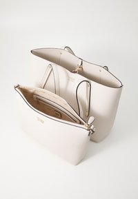 Béžová texturovaná kožená taška Guess s odpovídajícím zipovým pouzdrem, zlatými kovovými doplňky a brandovanou vnitřní podšívkou.