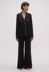 Mustast pajamasest komplekt, mis sisaldab pika varrukaga nööbitavat särk ning ühe rinnataskuga, valgete äärejoontega, koos laia jalaga pükstega. Pehme tekstuur.