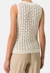 Top senza maniche lavorato a maglia in crema, con un motivo a intreccio aperto, scollo a costine e orlo. Abbinato a pantaloni beige chiaro, che mettono in risalto il contrasto di texture.