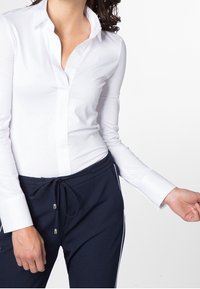 Camicia bianca a maniche lunghe con colletto classico, abbinata a pantaloni navy con cordoncino in vita, caratterizzati da strisce laterali e una vestibilità morbida.