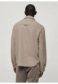 Beige textuurjacket met een getailleerde pasvorm, voorzien van een puntkraag, rugpand en knoopmanchetten. Glad stof en minimaal ontwerp.