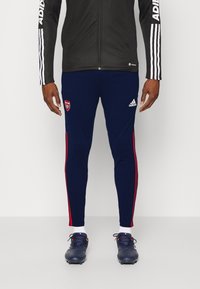 Námořnické sportovní kalhoty s červenými bočními pruhy, se znakem Arsenalu na levém stehně a vyrobené z elastického materiálu pro pohodlí.