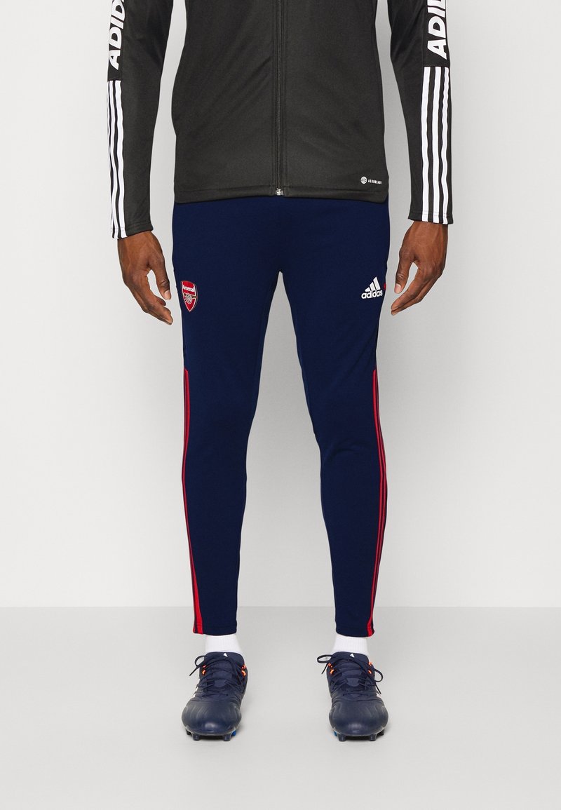 Námořnické sportovní kalhoty s červenými bočními pruhy, se znakem Arsenalu na levém stehně a vyrobené z elastického materiálu pro pohodlí.