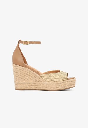 Kožené klinové sandále v hnedej farbe so zapleteným prírodným vláknom. Majú otvorenú špičku, remienok okolo členka so sponou a textúrovanú platformu.