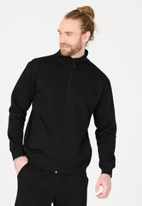 Sort zip-up sweatshirt lavet af glat stof, med høj krave, sidelommer og ribbede manchetter. Enkel design uden mønstre.