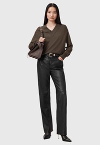 Maglione verde oliva a scollo a V, pantaloni larghi in pelle nera, borsa strutturata grigia e scarpe con tacco nere a punta con dettagli dorati.