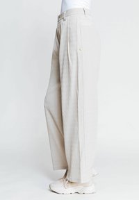 Breite, hellbeige Cordhose mit vertikalen Rippungen, ausgestattet mit einer taillierten Taille und einem einzelnen Knopfdetail an der Seite.