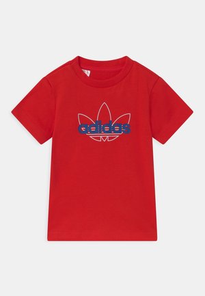 Rød t-shirt med korte ærmer, blå Adidas-logo og indrammet trefoil-design på brystet, vist på en ensfarvet baggrund.