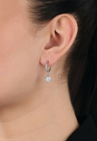 Orecchini a cerchio in argento con un cristallo rotondo pendente in una montatura a griffe, caratterizzati da una finitura lucida e da un design semplice ed elegante.