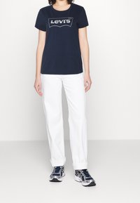 Tmavě modré tričko s stříbrným logem Levi's, kombinované s bílými rovnými kalhotami a tmavě modrými teniskami. Ležérní design, krátké rukávy, kulatý výstřih.