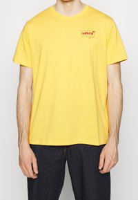 T-shirt di cotone giallo con un piccolo logo rosso Levi's sul lato sinistro del petto. Maniche corte, scollatura rotonda e vestibilità rilassata.