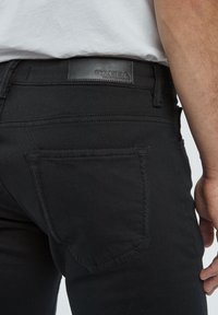 Jeans neri con una finitura testurizzata, caratterizzati da una patch in pelle in vita e una singola tasca posteriore con dettagli di cucitura visibili.