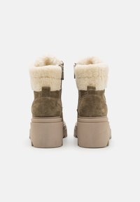 Bottes chelsea en daim marron avec un large col en fausse fourrure crème, dotées d'une fermeture éclair sur le côté et d'un large talon beige.
