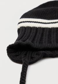 Bonnet en tricot noir avec des rayures blanches. Présente une texture côtelée et un lien tressé. Forme ronde avec une finition douce sur le bord.