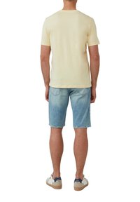 Hellgelbes T-Shirt mit kurzen Ärmeln, kombiniert mit hellblauen Jeansshorts. Die Schuhe sind weiß mit marineblauen Akzenten und braunen Sohlen.