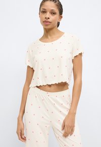 Λευκή cropped μπλούζα με ριγέ ύφασμα και ροζ σχέδια καρδιές, με κυματιστές άκρες, σετ με παντελόνι που ταιριάζει. Απαλό ύφασμα και άνετη εφαρμογή.