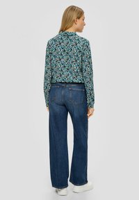 Blusa a fiori in turchese, nero e bianco, abbinata a jeans a gamba larga scuri a vita alta e sneakers bianche con la piattaforma.