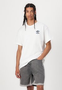 Hvit bomulls T-skjorte med blå Adidas-logo på brystet, kombinert med grå denimshorts med en falmet tekstur og vanlig passform.