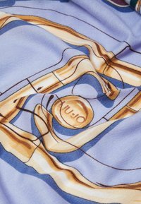 Tessuto blu morbido con una grafica di trombone, caratterizzato da accenti dorati e marroni e un dettaglio circolare del logo. Texture liscia, colori vivaci.