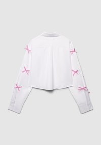 White cropped shirt with long sleeves, featuring pink ribbon accents on both arms, smooth texture, and a classic collar design.