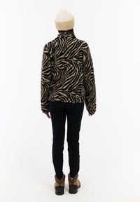 Osoba koja nosi bež pleteni šešir, crnu i bež duksericu s uzorkom zebra, crne hlače i smeđe planinarske čizme, stoji okrenuta leđima.