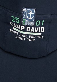 Tissu marine avec texte vert et blanc « 25 01 Camp David Right Sail for the Right Trip » et un patch bleu affichant un symbole d’ancre.